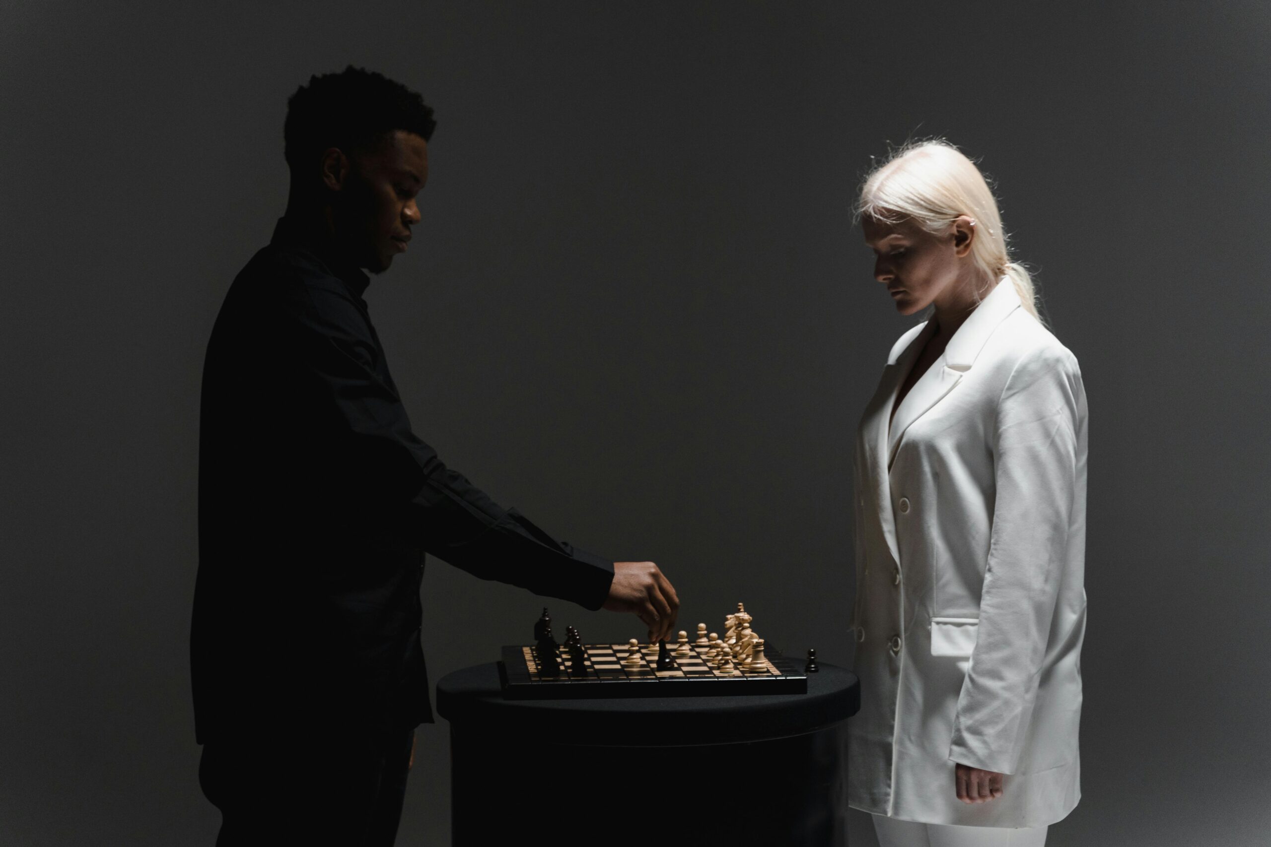 Two people engaged in a strategic chess match, silhouetted against moody studio lighting.