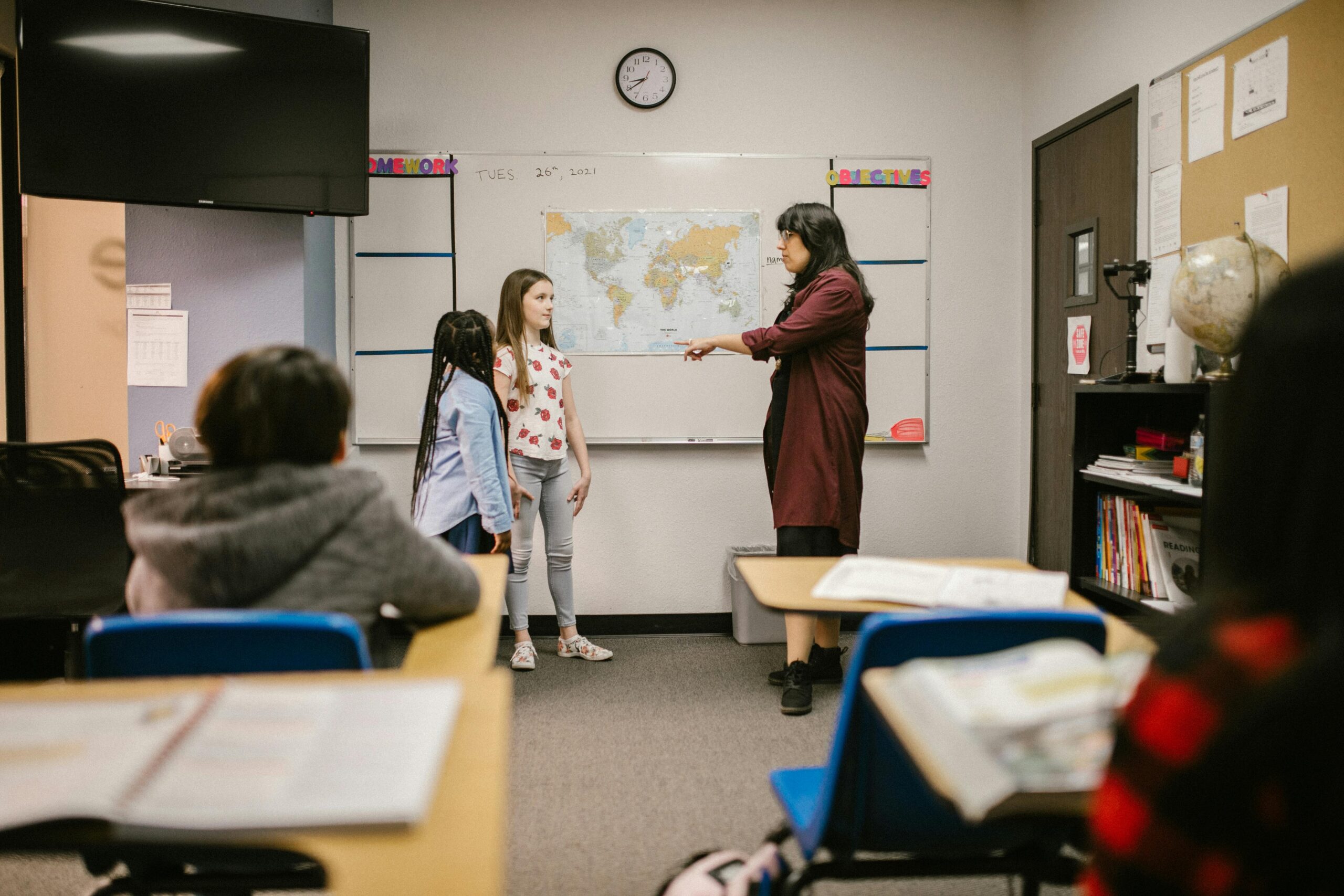 A teacher instructs students in a classroom with a world map and educational materials.