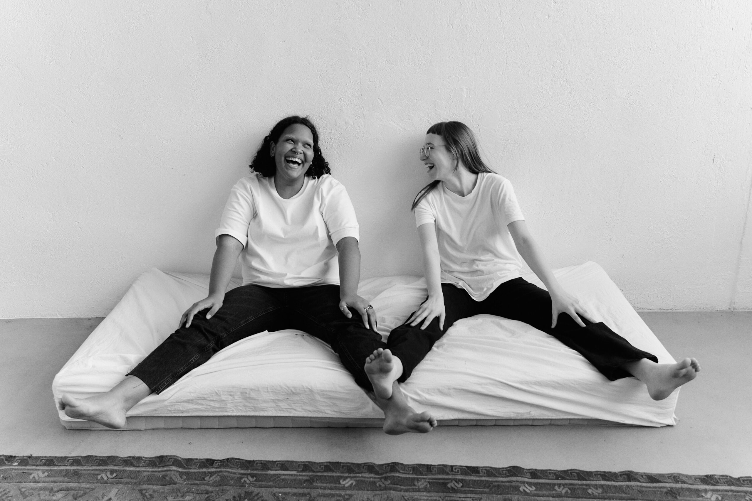 Black and white photo of two women laughing on a bed, showcasing friendship and happiness.