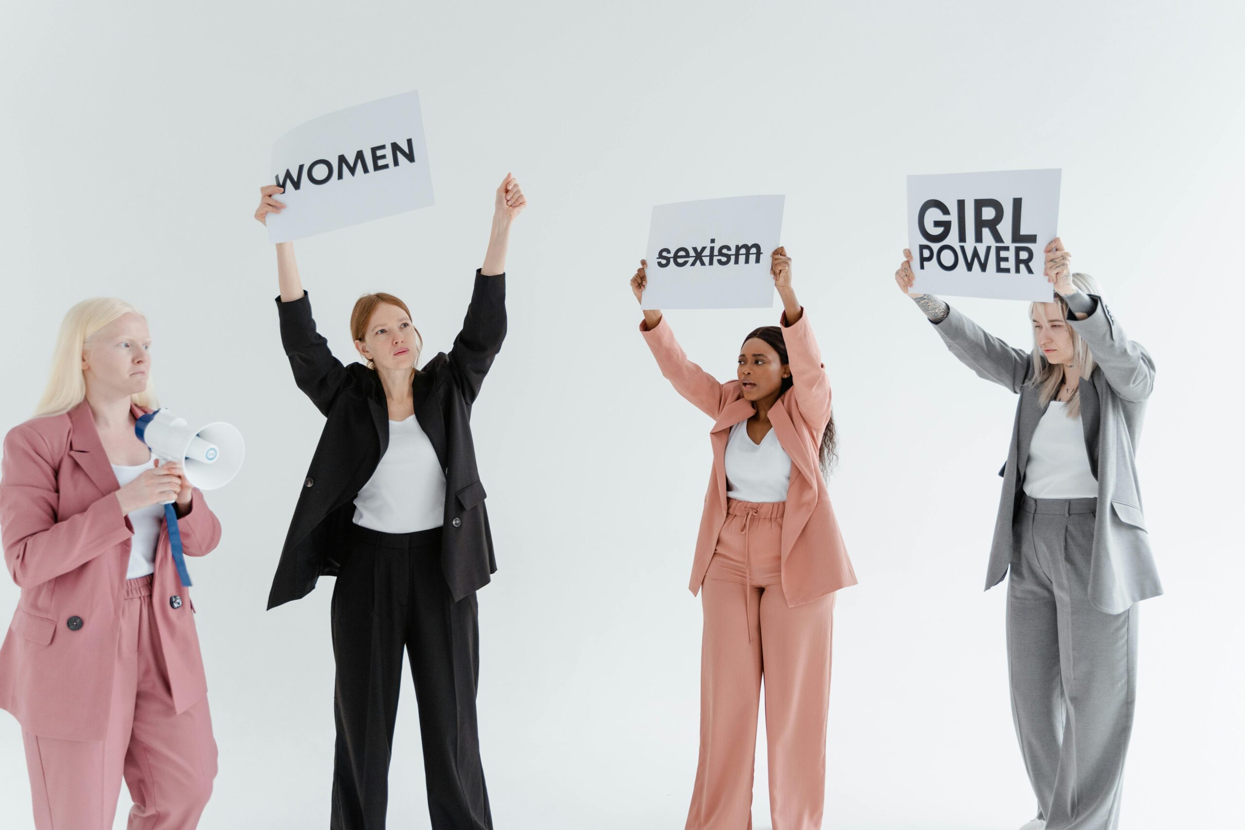 Four women in formal wear hold signs advocating for gender equality and empowerment.